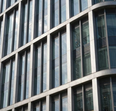 A close-up photograph of a modern building facade featuring premium glass and steel textures. The composition is sharp and architectural, showcasing sophisticated construction quality under bright daylight in a South Asian city.