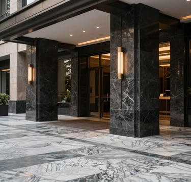 A detailed close-up of a modern building entrance in a South Asian city, featuring high-quality marble flooring and charcoal-colored architectural pillars with warm accent lighting.