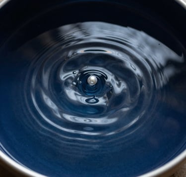 A minimalist composition showing a single ripple in a bowl of dark water. The water is a Deep Midnight Blue, and the ripple reflects Pearl White light. This represents the concept of internal stillness and the sound of the soul.