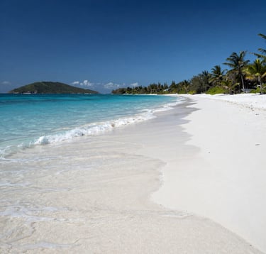 A high-end landscape photograph of a pristine white-sand beach in the US Virgin Islands. Crystal clear light blue water laps the shore under a bright navy sky, reflecting a sense of sophisticated tranquility and adventure.
