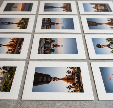 An editorial close-up photograph of high-end photography prints laid out on a soft gray stone surface. The composition is strictly grid-based and highly organized. Soft, natural daylight illuminates the textures of the archival paper. Global / Contemporary Art setting. The mood is professional and curated, using a palette of off-white and muted tones.