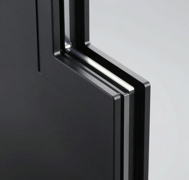 Macro photography of a sleek, ultra-thin window profile. The material is matte black aluminum with a refined texture. Soft, diffused studio lighting emphasizes the sharp angles and precision engineering.