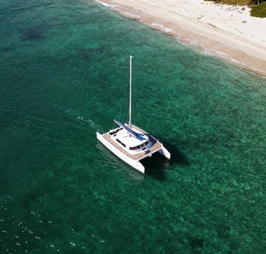 An aerial view of a private catamaran sailing through the crystal clear waters of an archipelago in Brazil, dark green water, white sand, exclusive South American / Brazilian travel mood.
