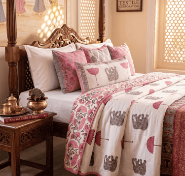Traditional hand block print Indian bedding set with pink floral and elephant patterns on a carved wooden bed.