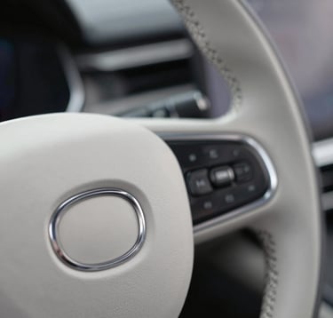 Macro shot of a high-end luxury car steering wheel, focusing on the fine leather stitching and the metallic logo. Minimalist composition with #CECECE and #272635 colors.