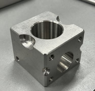 A sharp, detailed photograph of a precision-machined steel alloy component with a brushed metal finish, showcasing intricate CNC-cut details and sharp edges, resting on a professional gray workshop bench.