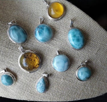 Dijes de piedras preciosas como Larimar y Ámbar sobre una superficie con textura color crema.