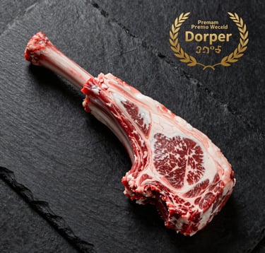 Top-down professional culinary shot of a raw, vacuum-sealed premium Dorper lamb cut on a black slate surface. The packaging is minimal and elegant with gold branding. Crisp, clean lighting emphasizes the marbling of the meat. Colors: black, deep red, and gold.