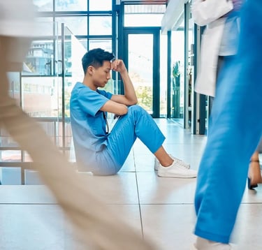 An exhausted nurse in blue clothing sitting on the floor thinking