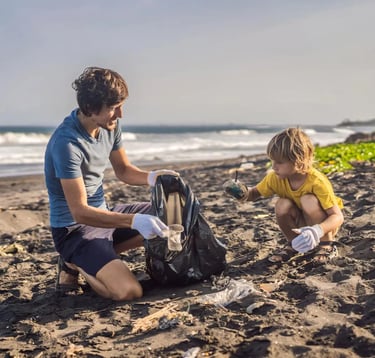 A father and his son sitting on the beach, collecting garbage into a black plastic bag