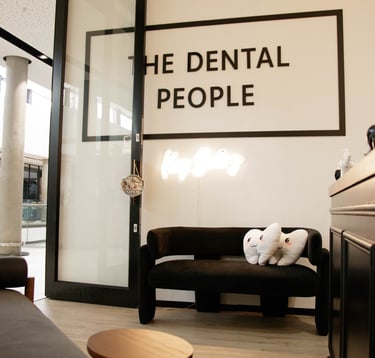 The Dental People office waiting area with tooth-shaped pillows on a black couch and neon sign.
