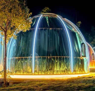 غرفة زجاجية على شكل فقاعة شفافة مضاءة ليلاً وسط الطبيعة، مهيأة لجلسة طعام خاصة