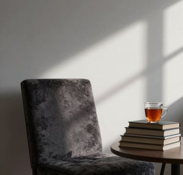 A quiet, moody library corner with a single high-back velvet chair. A stack of books sits on a side table next to a cooling cup of tea. Shadows play across the walls. Colors: #4A5F5C, #1C2826.