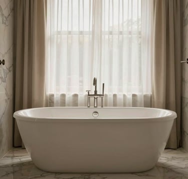 Professional photography of a freestanding soaking tub in a modern Los Angeles bathroom. The tub is positioned near a window with soft, sheer curtains, creating a serene and luxurious spa-inspired scene with soft beige and marble gray tones.