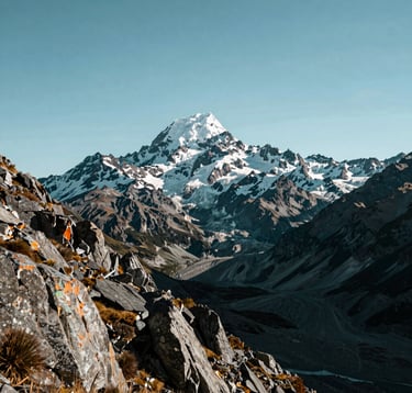 A majestic view of Aoraki Mount Cook under a clear sky, Oceania / New Zealand. The composition focuses on the rugged mountain textures and the vastness of the Southern Alps. The scene is peaceful and high-end, using deep teal and light blue tones.