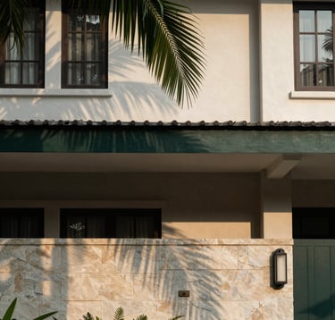 Close-up architectural photography of a modern residential facade in Sooko, East Java. Use of natural stone and dark green accents. Soft morning lighting with shadows of palm leaves, creating a calm and elegant atmosphere. Southeast Asian / Indonesian residential setting.