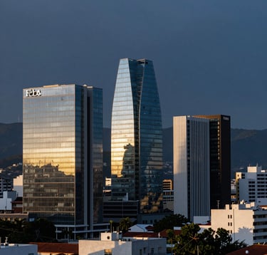 A panoramic, high-resolution view of the skyline of Cuenca, Ecuador during the golden hour. Modern glass buildings reflecting a deep dark blue sky, representing innovation and local growth with a Forbes-style aesthetic.