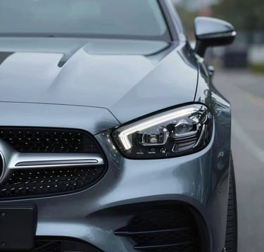 A close-up shot of the front grille and headlight of a luxury European car. The design is sharp and aggressive. The lighting is cold and professional, utilizing #B8CEDE for the metallic glints and #0A1128 for the deep recesses.