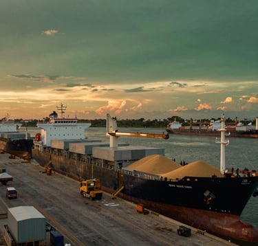 A wide-angle shot of a modern Brazilian port facility at sunset, where large cargo ships are being loaded with grain for export. The lighting is dramatic with deep green and orange hues, conveying global scale and economic strength.
