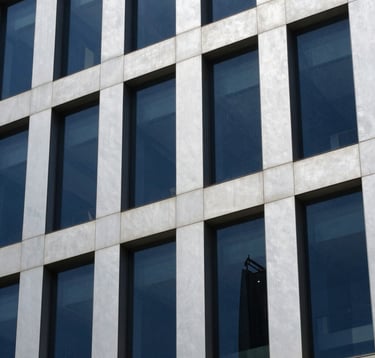 Close-up detail of a modern commercial office building in Bangalore. The facade uses Soft Silver panels and Dark Navy Blue tinted glass. The style is professional and elegant, captured in bright daylight.