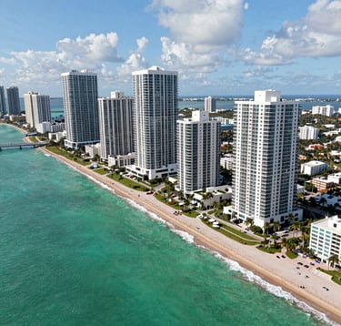 Aerial view of Sunny Isles Beach, luxury skyscrapers along the turquoise coast, South American / Latino vacation atmosphere, bright daylight, vibrant emerald water, professional real estate photography showing upscale living.