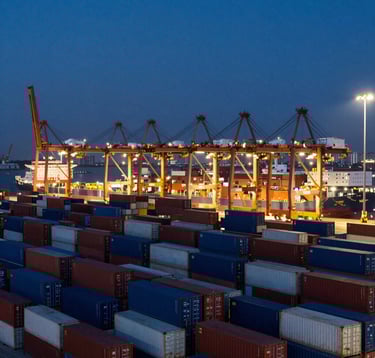 A professional corporate landscape showing a massive logistics port at night with rows of containers. The scene is dominated by dark navy blue tones with brilliant gold points of light from the cranes and ships.