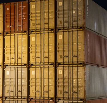 A close-up photograph of golden-lit shipping containers stacked neatly at a major Indian container port at night. The focus is on the precision and corporate efficiency of modern logistics.