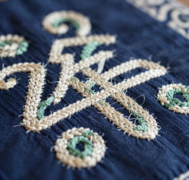 A focused shot of intricate Dao embroidery patterns on dark indigo fabric. The threads highlight colors from the palette like cream (#F5F5EC) and soft green. The texture of the hand-woven textile is visible, symbolizing the cooperative's commitment to cultural craft preservation.