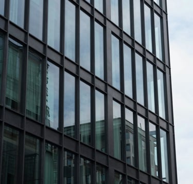 A close-up shot of an architecturally impressive modern building made of glass and steel, reflecting a clear sky. The style is minimalist and high-end, incorporating dark charcoal and forest green reflections, symbolizing stability and modernity.