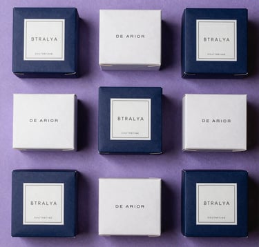 A top-down professional flat lay of high-end beauty product packaging with minimalist branding in a North American / US luxury spa setting. Soft purple and deep indigo color palette with elegant lighting.
