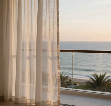Professional photography of a luxury resort balcony at sunset, soft warm light hitting white linen curtains, overlooking a calm ocean, minimalist and high-end aesthetic, North American / US luxury travel style.