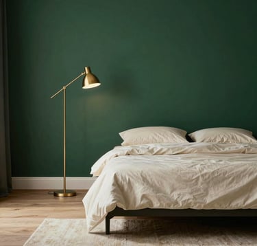 A serene and minimalist master bedroom. A low-profile bed with cream-colored linens is set against a royal dark green feature wall. To the side, a metallic gold floor lamp provides soft illumination. The flooring is light-toned wood with a soft beige plush rug.