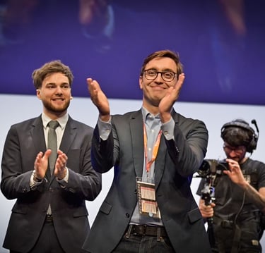 Two business professional men in suits clapping on stage during a corporate event or conference.