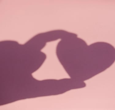 Sur fond rose, ombre d'une main qui tient avec deux doigts un coeur