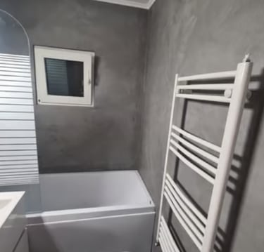 Casa de banho moderna com paredes em microcimento cinzento, banheira branca e toalheiro aquecido.