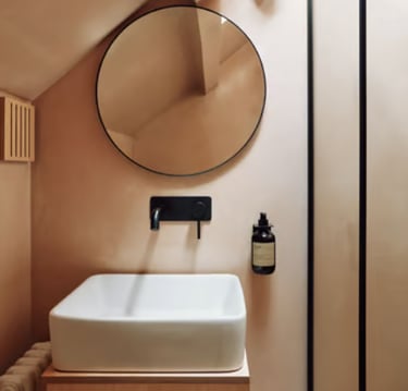 Modern bathroom with beige microcement walls, white washbasin, black wall-mounted tap and round mirr