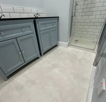 Modern bathroom with microcement flooring and walls, double blue cabinets and walk-in shower with wh