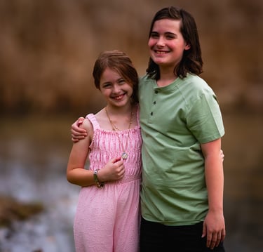 Two happy children, a girl in a pink jumpsuit and a boy in a green shirt, smile at Dow Lake Athens 