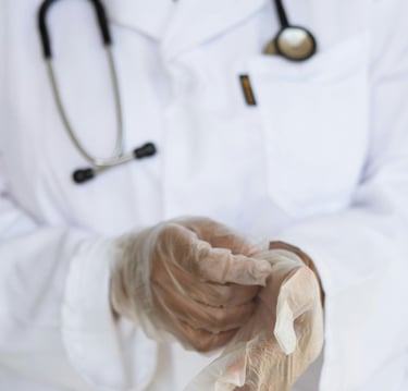A healthcare professional in a white lab coat putting on sterile medical gloves for a procedure.