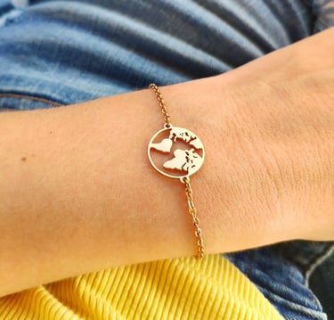 Dainty gold chain bracelet featuring a circular world map globe charm on a person's wrist.