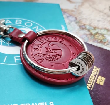Red leather Vagabond Life travel keychain with silver rings on a passport and world map.