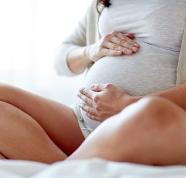a pregnant woman holding her belly while sitting on a bed