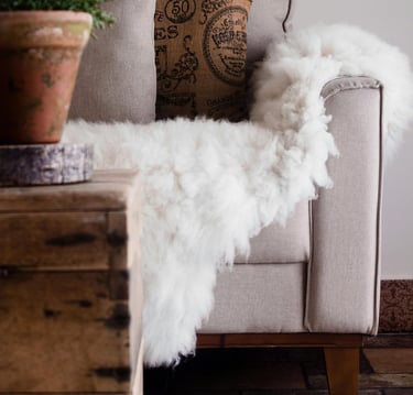 Cream upholstered chair styled with patterned throw pillow and faux fur throw blanket