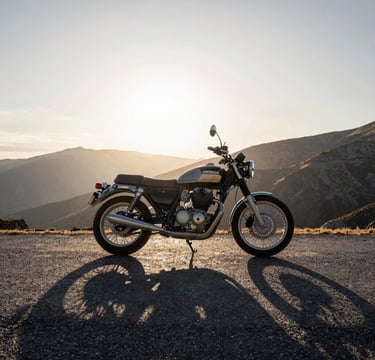 A wide-angle, cinematic photograph of a classic motorcycle parked on a high mountain pass in a Global / Western landscape. The lighting is low-sun golden hour, casting long shadows of deep charcoal across the pavement. The sky is a gradient of frost white and silver grey. Sophisticated and adventurous mood.