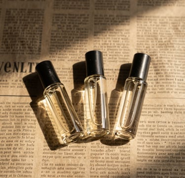 Overhead flat-lay of three small glass perfume vials resting on a vintage newspaper, sharp studio shadows, warm golden light