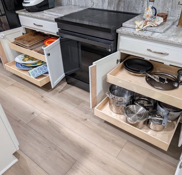 Two kitchen cabinets are open with glide out shelves extended out and filled with pots, pans and dishes. Better use of space!