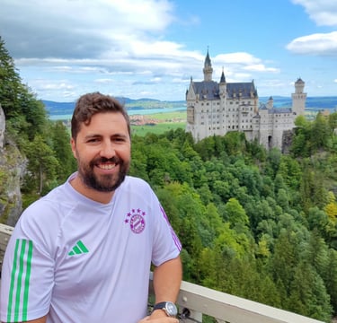 Smiling man in a white soccer jersey at Neuschwanstein Castle viewpoint in Germany.