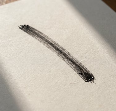 A high-detail, artistic close-up photograph of a piece of thick, textured watercolor paper with a single charcoal stroke. Soft natural morning light from the side creates a sophisticated and introspective mood. Colors include cream and charcoal. International / Western setting.