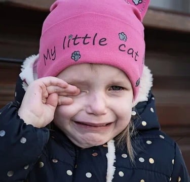 Enfant qui pleure avec bonnet rose (avec inscription My little cat) et doigts main droite sur l'oeil