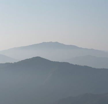 A minimalist wide-angle landscape photograph of misty mountains in the distance, featuring a soft grey and light blue color palette, clean composition, International / Western setting, high-end fine art style.